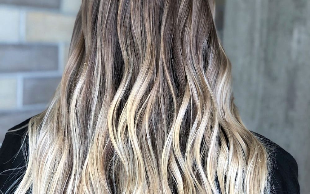 Long wavy hair painted from soft brown at the roots to bright blonde at the ends