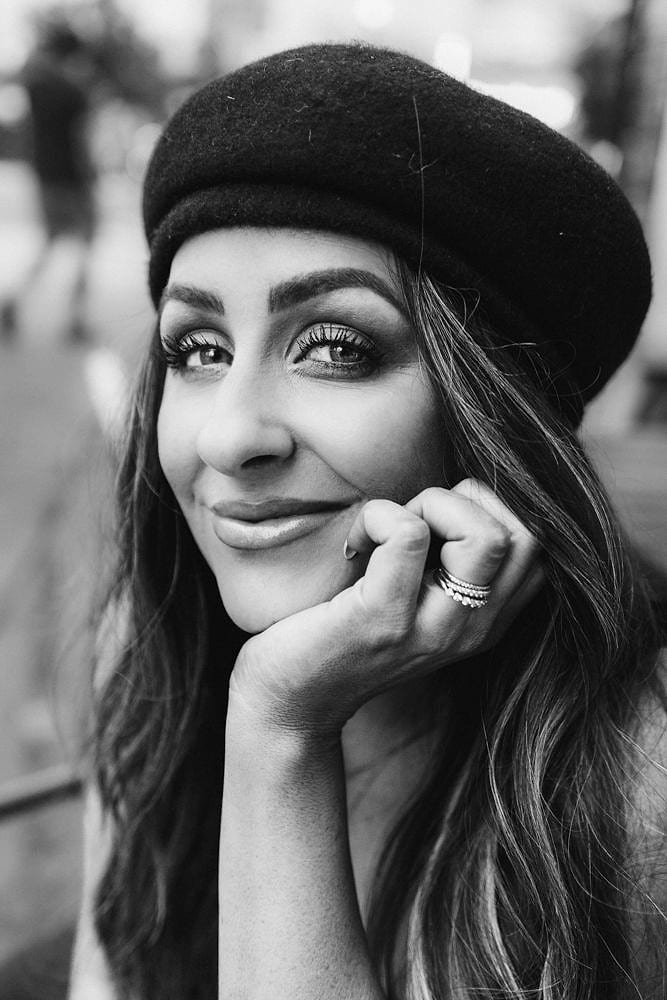 Black and white portrait of a smiling woman in a wool beret, resting her chin on her hand